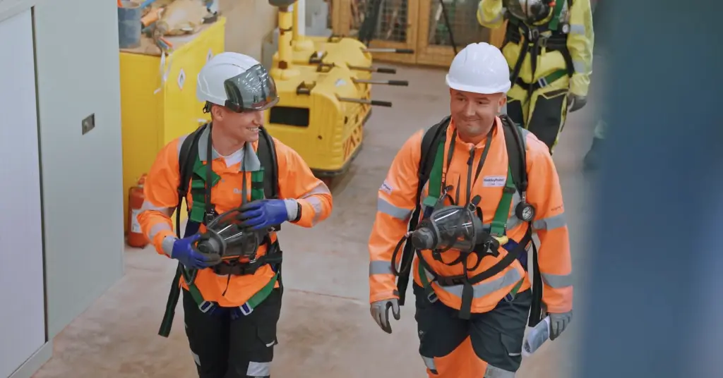 Two workers in safety harnesses and hard hats in an industrial building