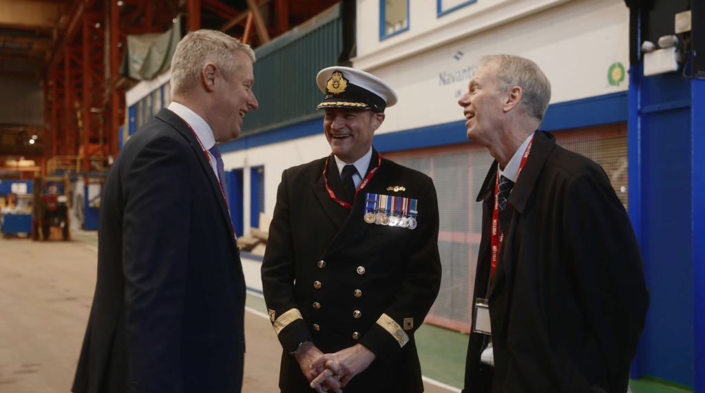 Naval officer talking with two men in a shipyard