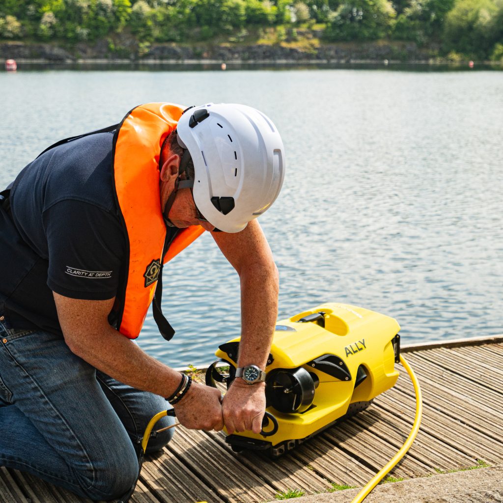 Technician in lifejacket and helmet connecting the tether to an inspection ROV