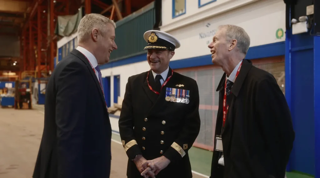 Naval officer and guests talking inside a dockyard building